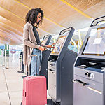 happy black woman using the check-in machine at the airport getting the boarding pass.