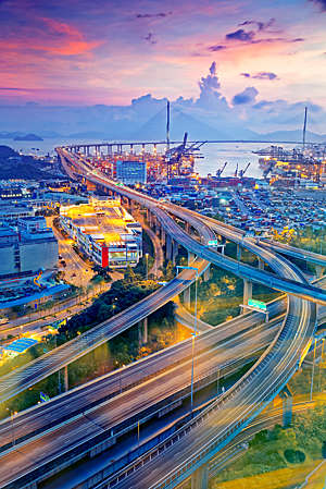 Container cargo freight ship with working crane bridge in shipyard at dusk.