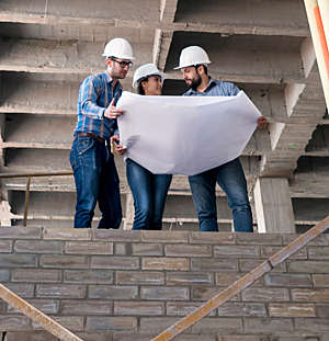 Three workers pore over a construction works plan at a building site.