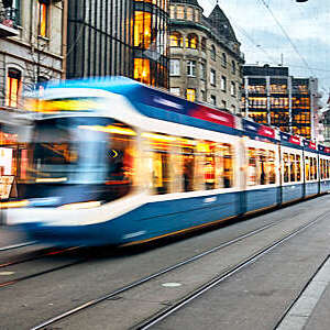 Blurred view of blue and white tram speeding across a city centre.