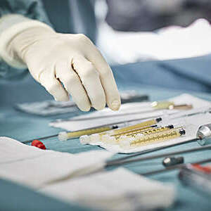 Close shot of a surgeon's gloved hand reaching for syringes on table.