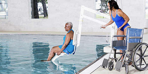 A physical therapist lowers a senior female patient into the pool using a spa lift. 