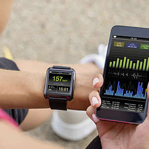 Close-up of woman’s hand synchronizing her mobile phone with the smart watch heart-rate monitor on her wrist.