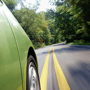 Hybrid economy car, a Prius, making tracks down a mountain road. Sign ahead indicates curvy highway. Car is sharp, landscape and street are motion-blurred (all in-camera).