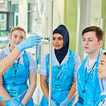 Four student nurses watch on as one student practices using an intravenous catheter.