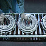 Overhead view of worker’s hands moving clutch pressure plates down the production line in an industrial clutch factory.