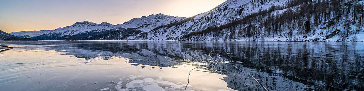 Piz Da La Margna mirrored in the frozen Lake Sils covered of ice bubbles, canton of Graubunden, Switzerland.