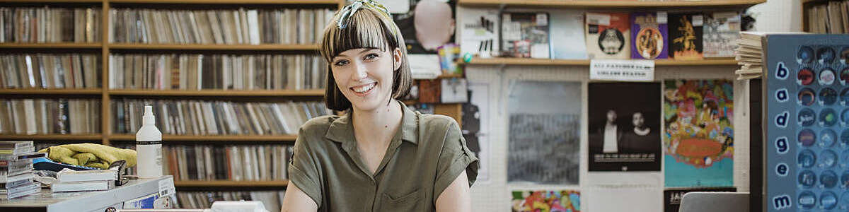 Portrait of a female retail worker standing behind the counter in a record store, smiling at camera.