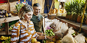 Medium shot of smiling couple picking out fruit at local market while on vacation